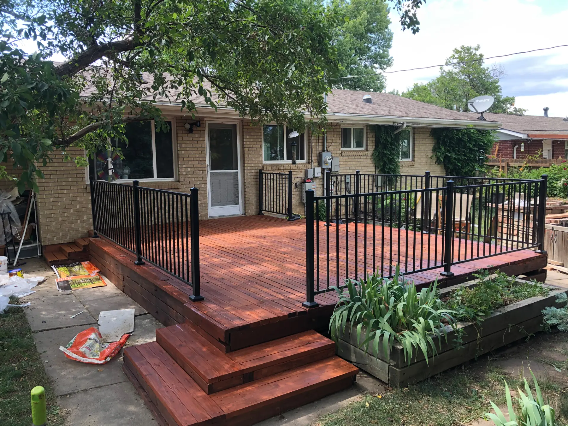 Backyard deck freshly stained rich red with black metal railing behind a brick home