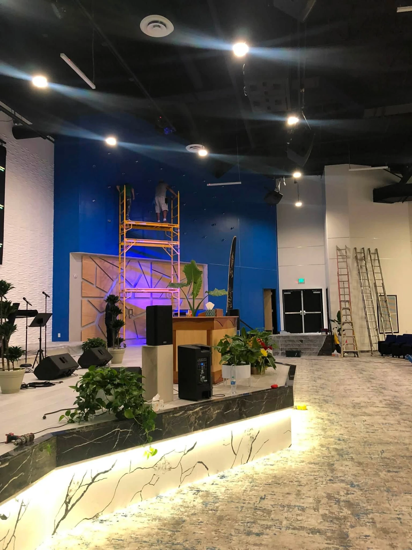 Crew painting a tall blue accent wall in a large church auditorium
